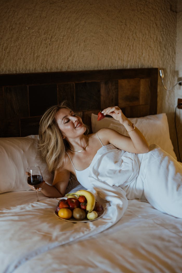 A woman laying on a bed with fruit and wine